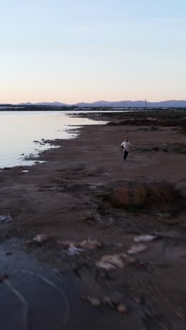 man walking along a tranquil lake shore at dusk