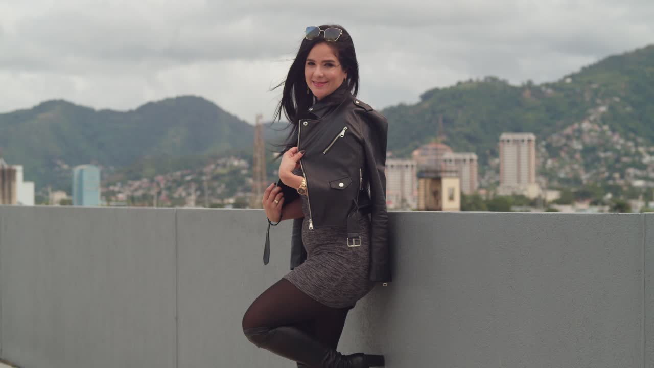 una mujer se está divirtiendo en un techo con el paisaje urbano de port of spain, trinidad, detrás de ella