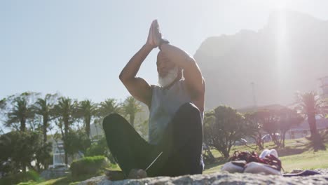 senior african american man exercising stretching on rocks by the sea