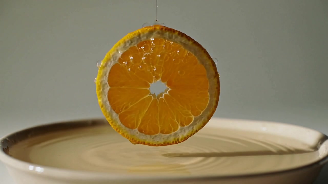 Goccioline che cadono e colpiscono una fetta di agrume su un filo sopra una ciotola d'acqua in studio, creando increspature