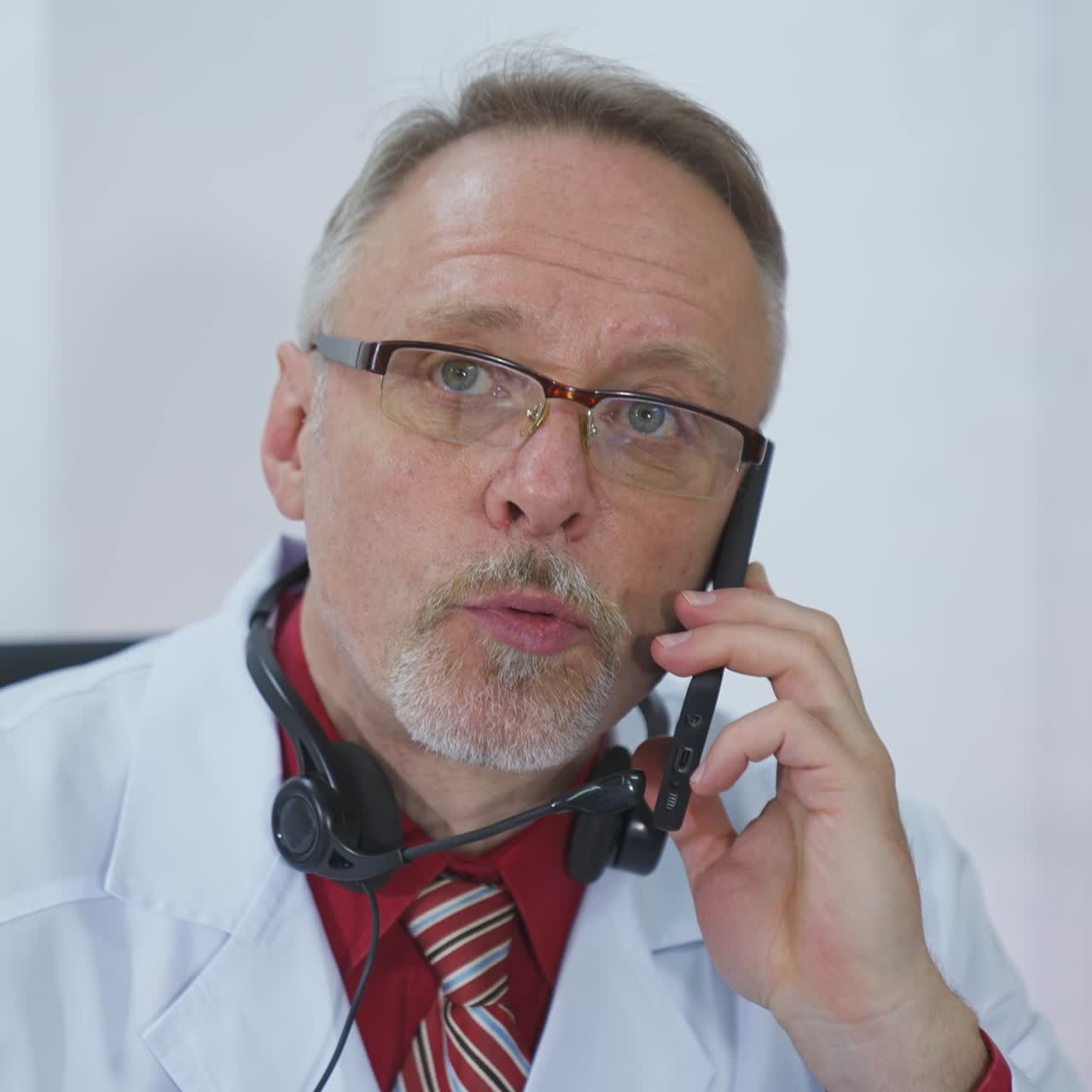 Medical consultation with a phone. Portrait of serious male doctor in lab coat talking on mobile phone in medical office. ?oncept of pandemic, modern medicine.
