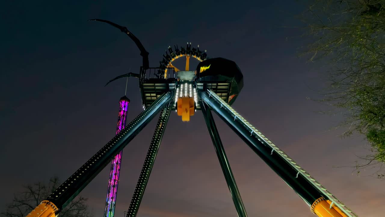 Static visual of a spider-shaped structure, amusement park game with round pendulum shape at night.