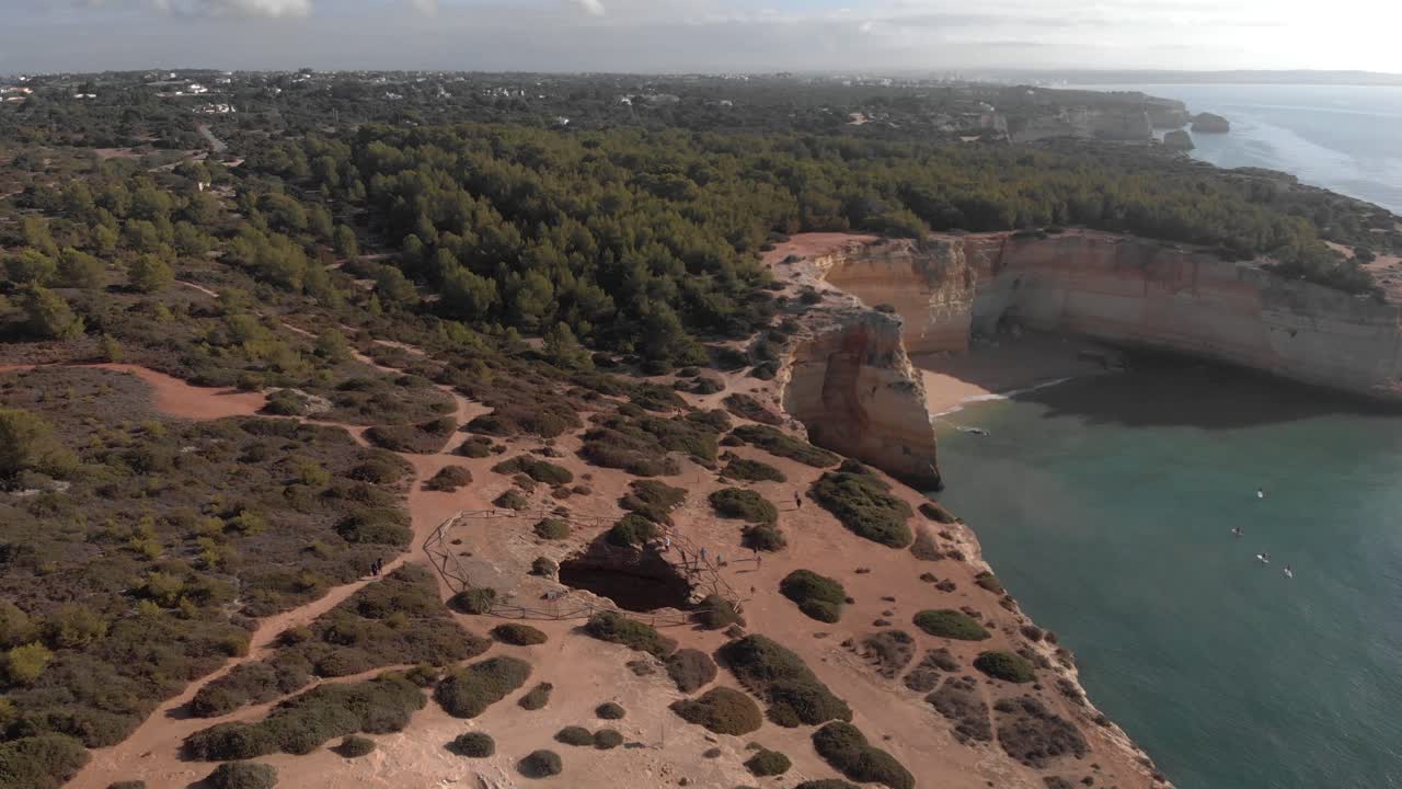 Fantastic aerial view of Benagil, beautiful mountains of sedimentary rocks, lots of green vegetation, calm sea with some boats docked, crystal clear water, nature is perfect. Aerial camera.
