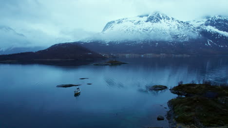 backwards aerial shot of a fishing boat in a norwegian fjord during late night in winter