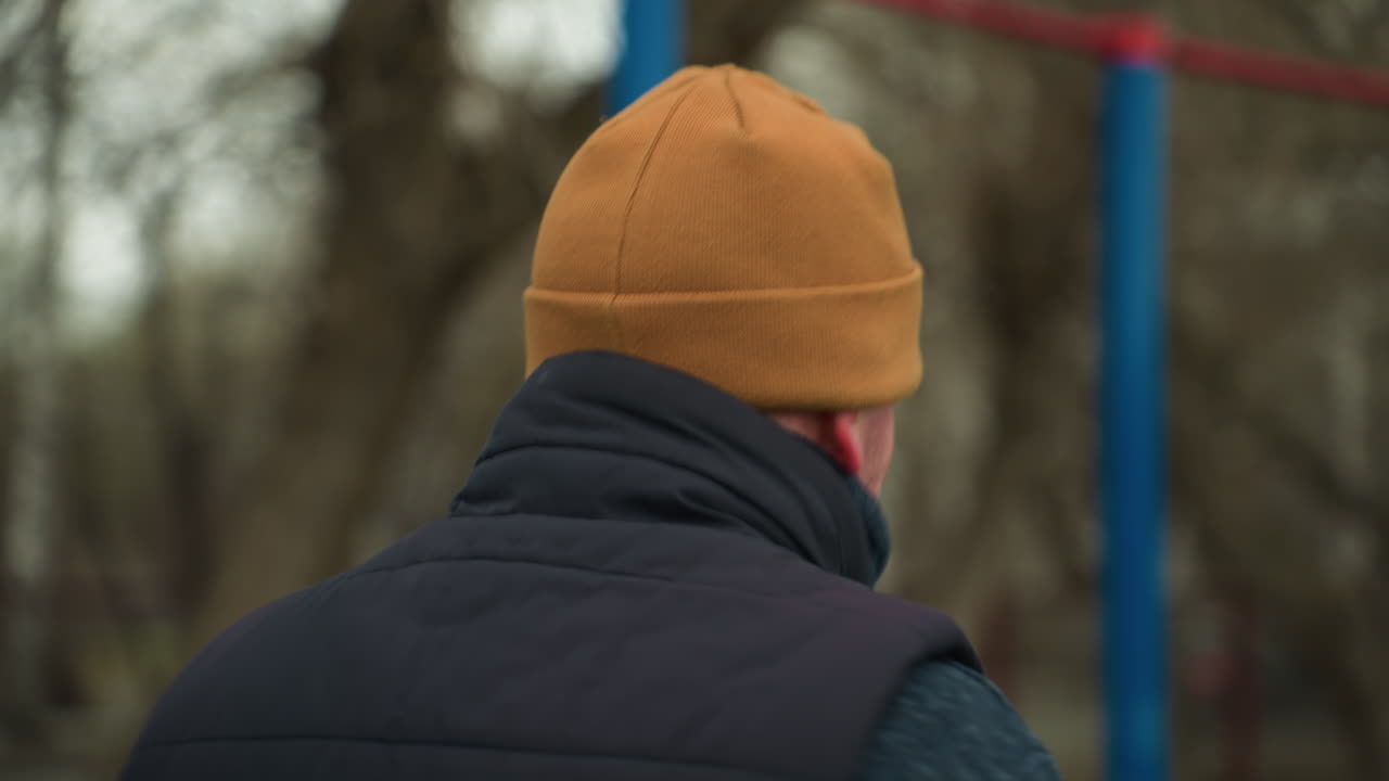 vista trasera de un entrenador corriendo rápidamente en un gimnasio al aire libre, con una vista borrosa de un coche pasando por la izquierda y barras de hierro rojas y azules en el fondo y árboles desnudos