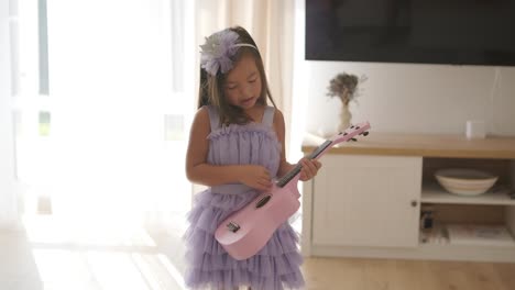 a beautiful little girl is playing the ukulele in the living room for her mom.