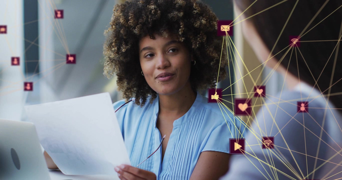 Woman raising specs, reading paper and speaking to peer in office network icons overlaying right