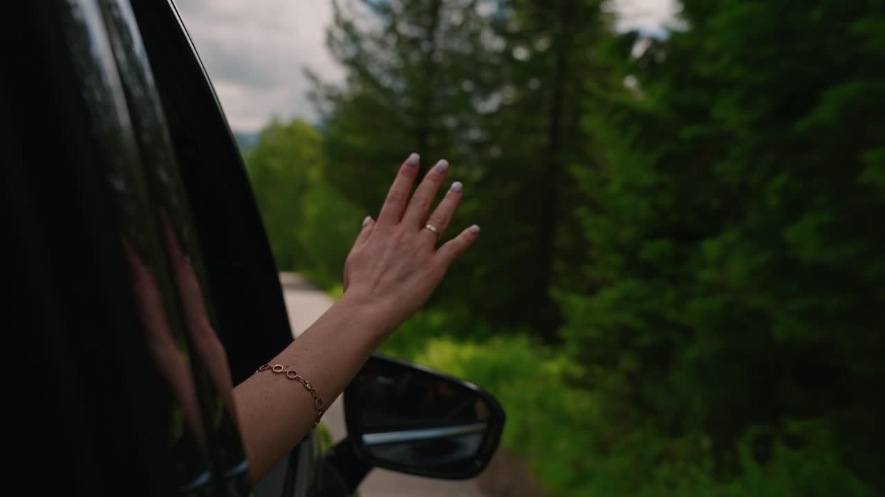 Woman's hand out of car window enjoying scenic drive