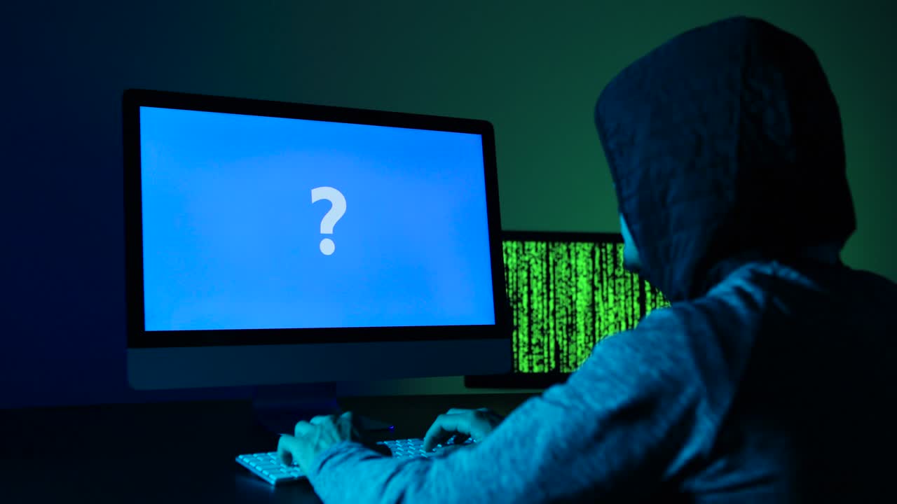 hombre sentado frente a una computadora con un mensaje de interrogatorio en la pantalla.