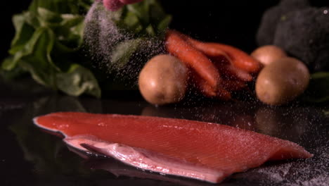 hand seasoning trout fillet in front of vegetable selection