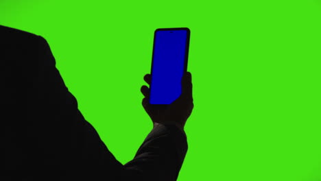 close up of businessman holding blue screen mobile phone standing against green screen background