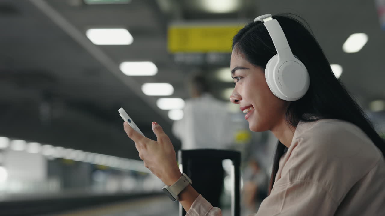 Woman using smartphone and headphones at train station