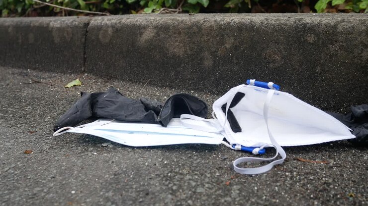 Dirty discarded used corona virus masks and gloves rubbish on street blowing in wind with copy space