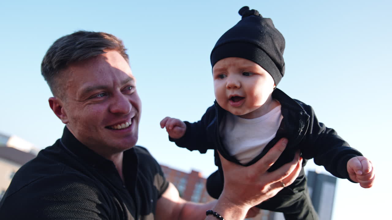 Face of Caucasian baby boy in a black cap. Smiling happy dad holding his child. Close up.