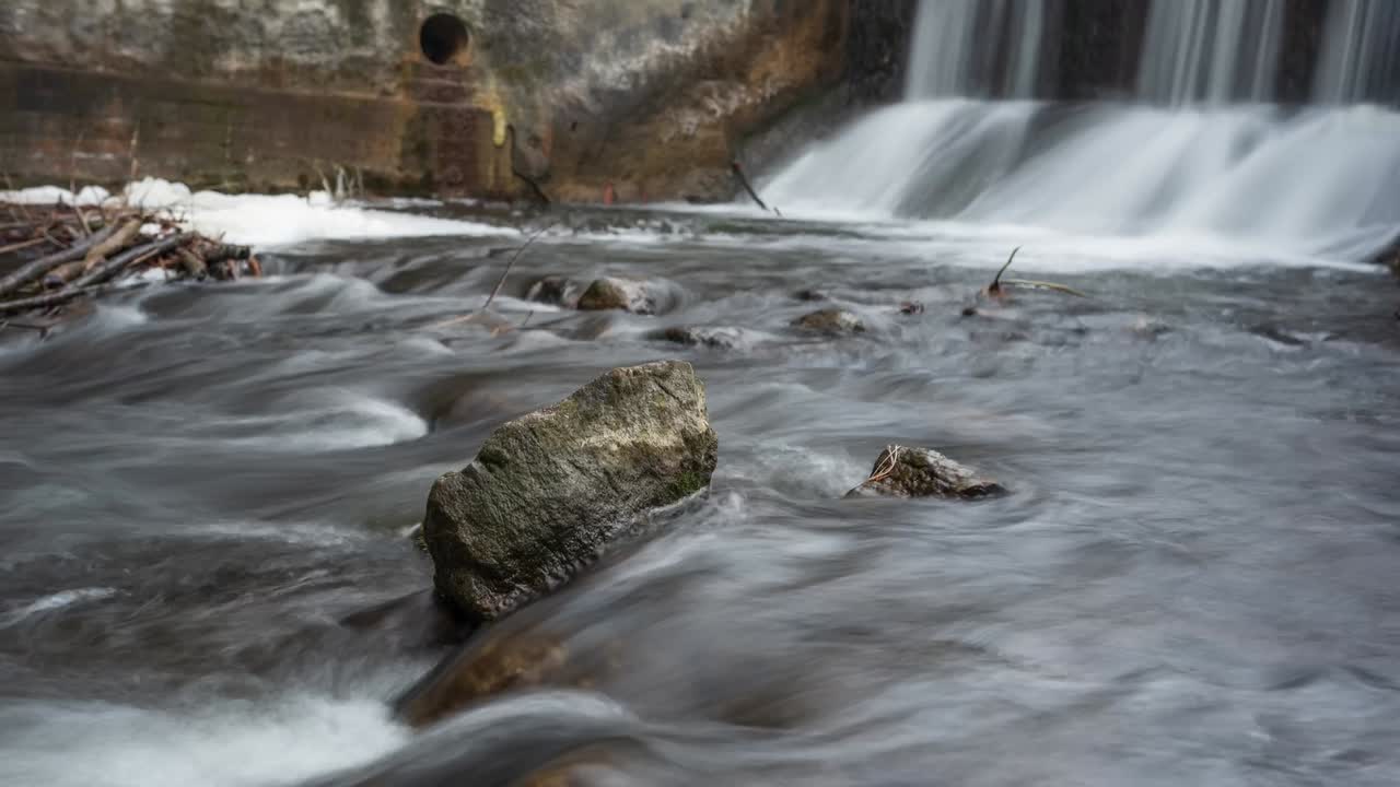 Winter river flowing over rocks below dam sluice waterfall, timelapse