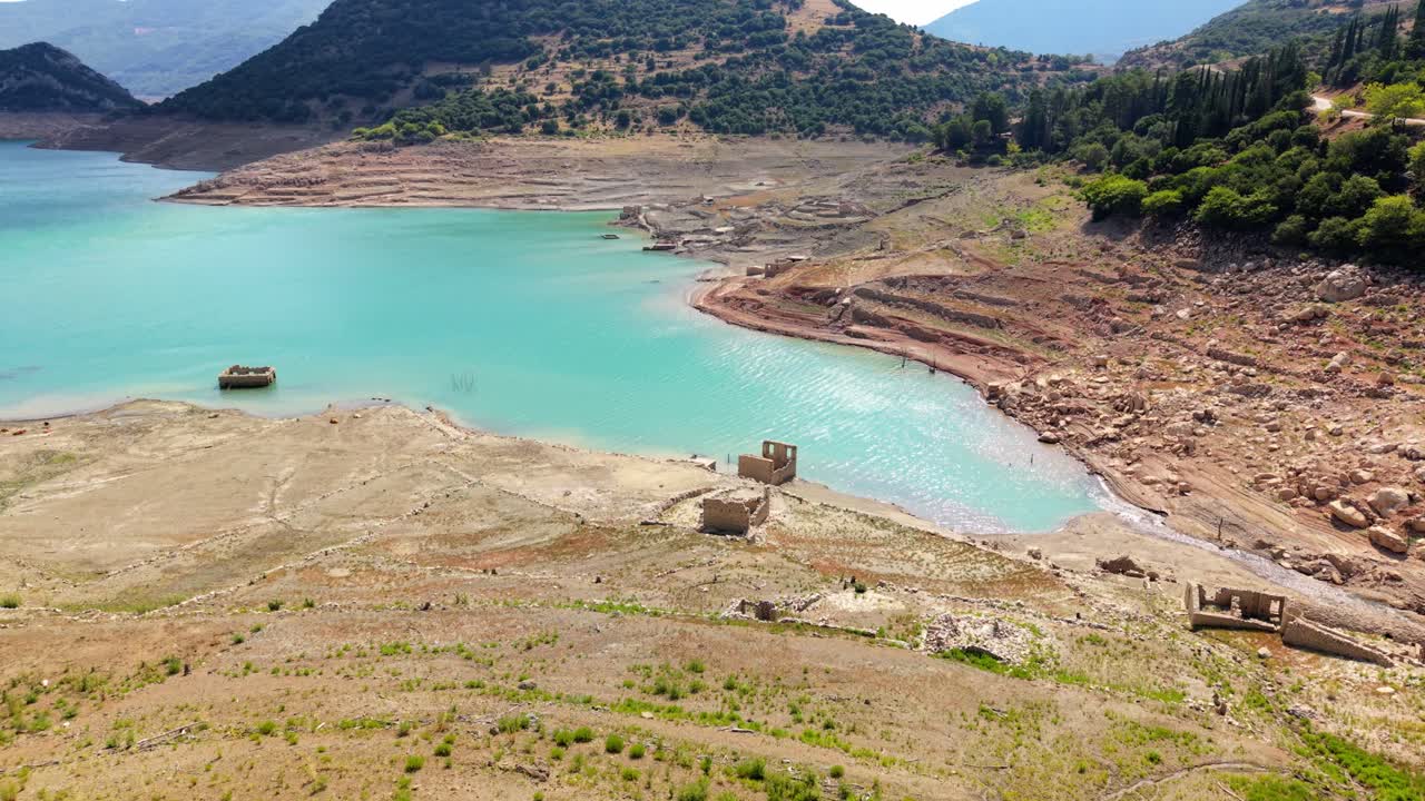 Transition from dry lake shore to bright turquoise reservoir surrounded by green forest