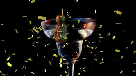 Golden-confetti-falling-over-olives-falling-into-cocktail-glass-against-black-background