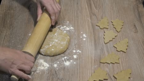 a woman rolls out a piece of yellow dough on a wooden table with a rolling pin. she prepares festive cookies in the form of a christmas tree. concept . close-up. the view from the top. faceless. 4k.