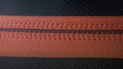 a cinematic macro close-up shot of a hard case zipper being opened, orange rexture, metal zip, black box, photography gear, professional studio lighting, static 4k video