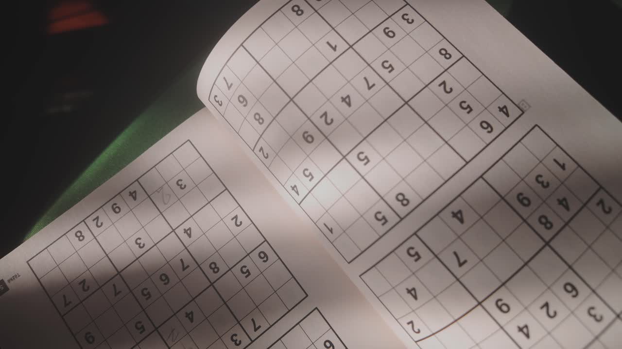 Soft light falls on open page of Sudoku puzzle book, lifestyle concept