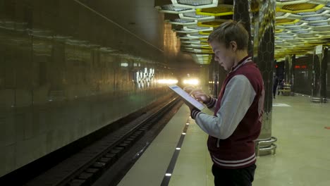 adolescente usando una tableta en una estación de metro ocupada