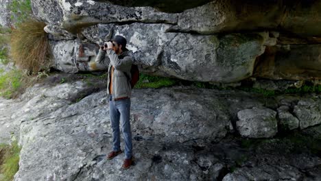 Männlicher-Wanderer-Blickt-Durch-Ein-Fernglas-In-Der-Nähe-Einer-Höhle-4k