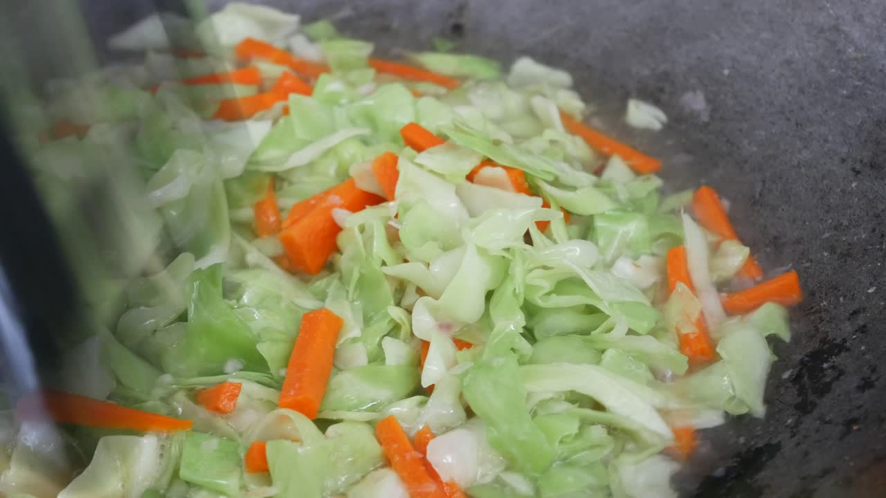 Fresh green cabbage is fried in a pan using hot cooking oil. Mix with carrot and chilli. Traditional Chinese cuisine