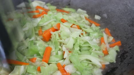 fresh green cabbage is fried in a pan using hot cooking oil. mix with carrot and chilli. traditional chinese cuisine