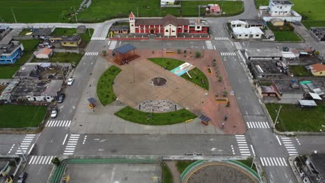 Cinematic-drone-clip-flying-over-a-park-towards-a-red-church-in-a-village-in-Chaupi,-Equador