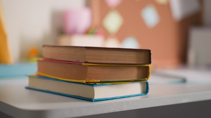 Studentessa mette una pila di libri di testo vicino al quaderno aperto sulla scrivania.