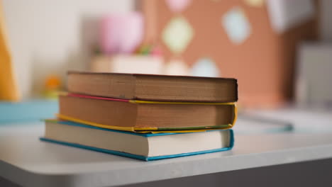 Girl-student-puts-textbooks-stack-near-open-copybook-on-desk