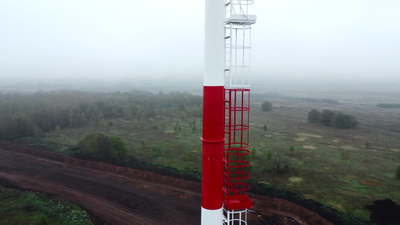 Dron desciende junto a una torre industrial roja y blanca en un paisaje neblinoso