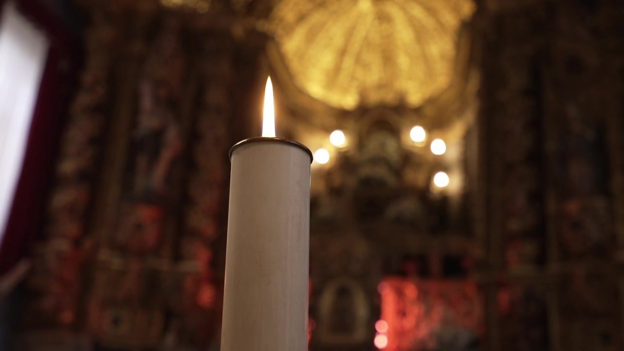 Candela accesa contro un interno di chiesa ornato e sfocato, che emana un bagliore caldo.
