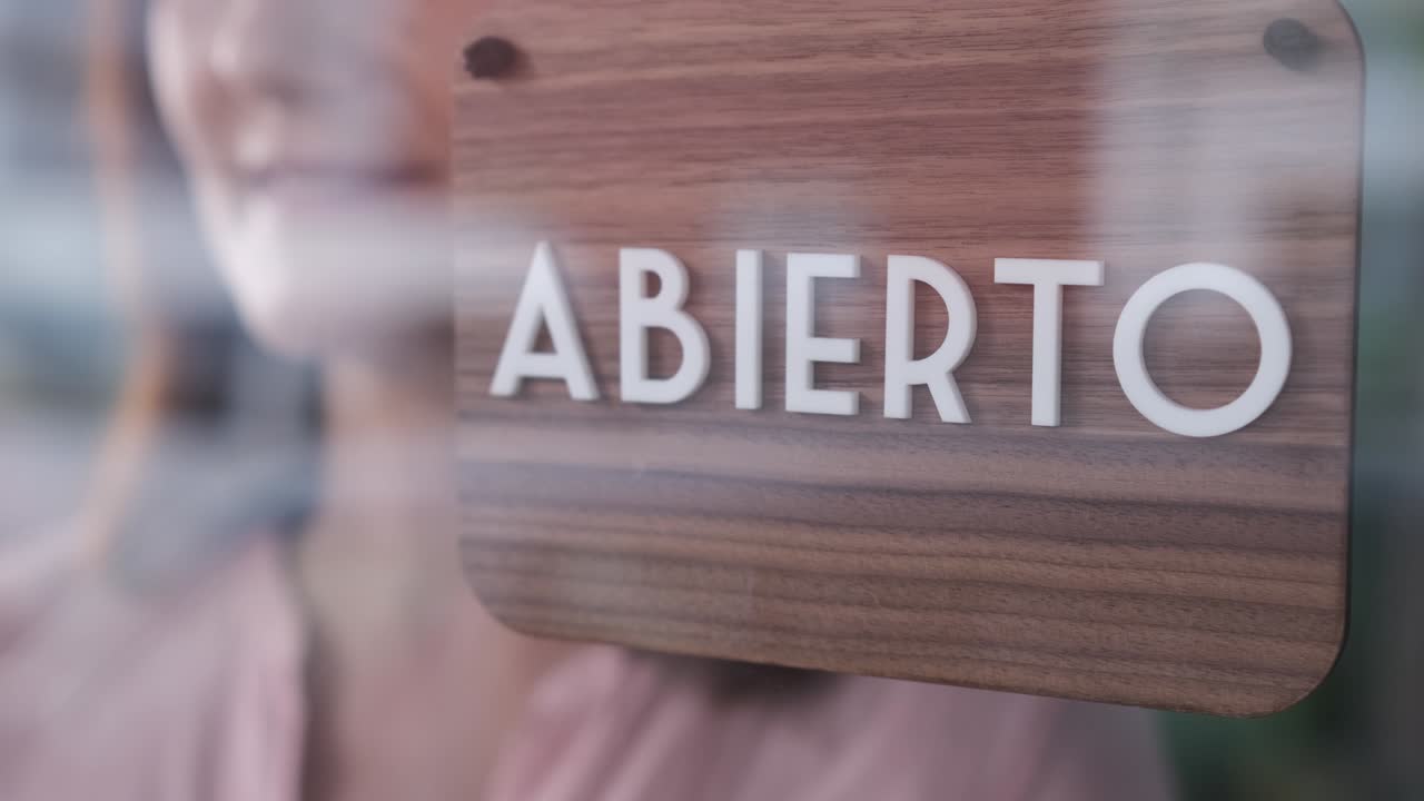 Happy woman changing closed to open sign in spanish, unrecognizable. Start-up concept. 4k 60fps
