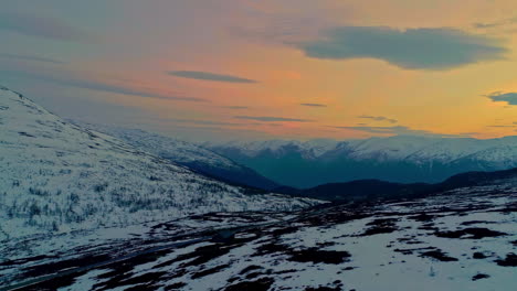 Toma-Panorámica-De-Drones-Aéreos-Sobre-Camino-Nevado-En-Montañas-Con-Cielo-Colorido-Al-Amanecer