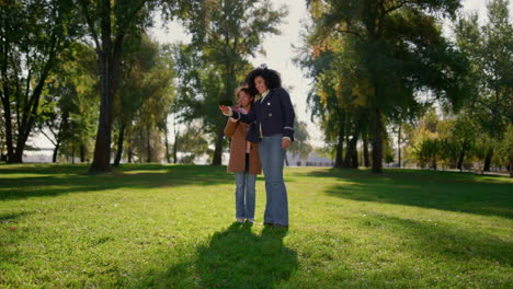 mamá sonriente haciendo una llamada en línea saludando a la cámara. familia feliz posando en el parque.