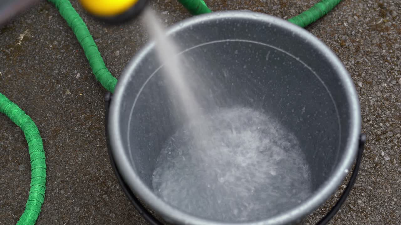 Acqua fresca che da un tubo viene spruzzata in un secchio, uno spreco.