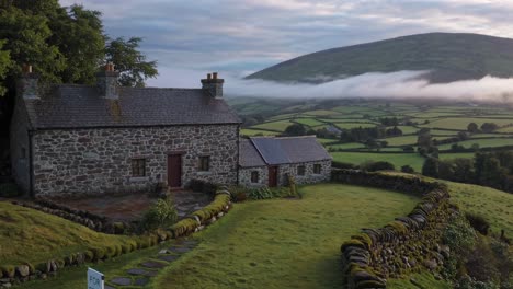 charming stone cottage available for rent, nestled in the serene countryside with breathtaking views of a misty valley and rolling hills bathed in the soft glow of early morning light