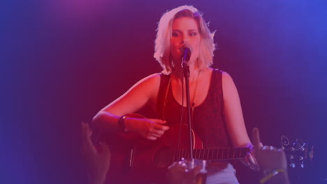 Animación-De-Puntos-De-Luz-Contra-Una-Cantante-Caucásica-Tocando-La-Guitarra-Y-Cantando-En-Un-Concierto