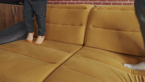 cropped body multiethnic father and toddler son jumping on couch