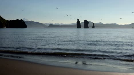 rocky islands in sea and beach of black volcanic sand on sunny day