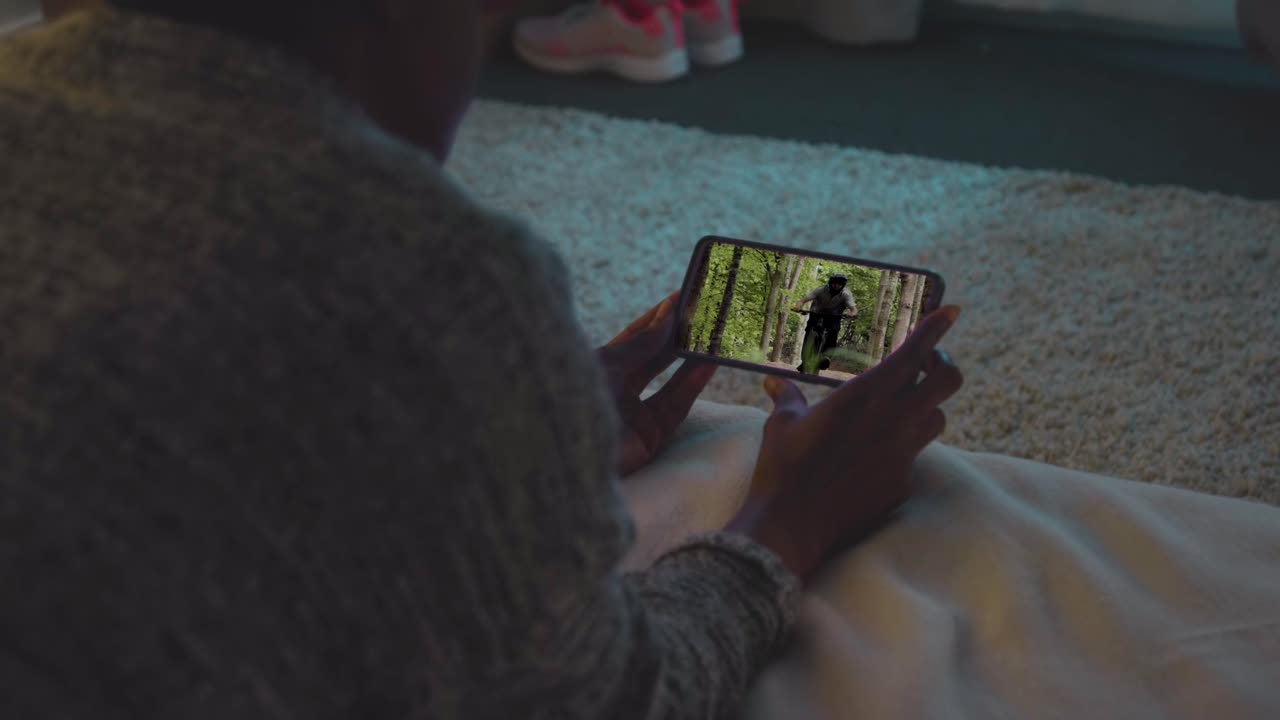 집에서 침대에 누워서 드폰으로 bmx 자전거 비디오를 보고 있는 여자