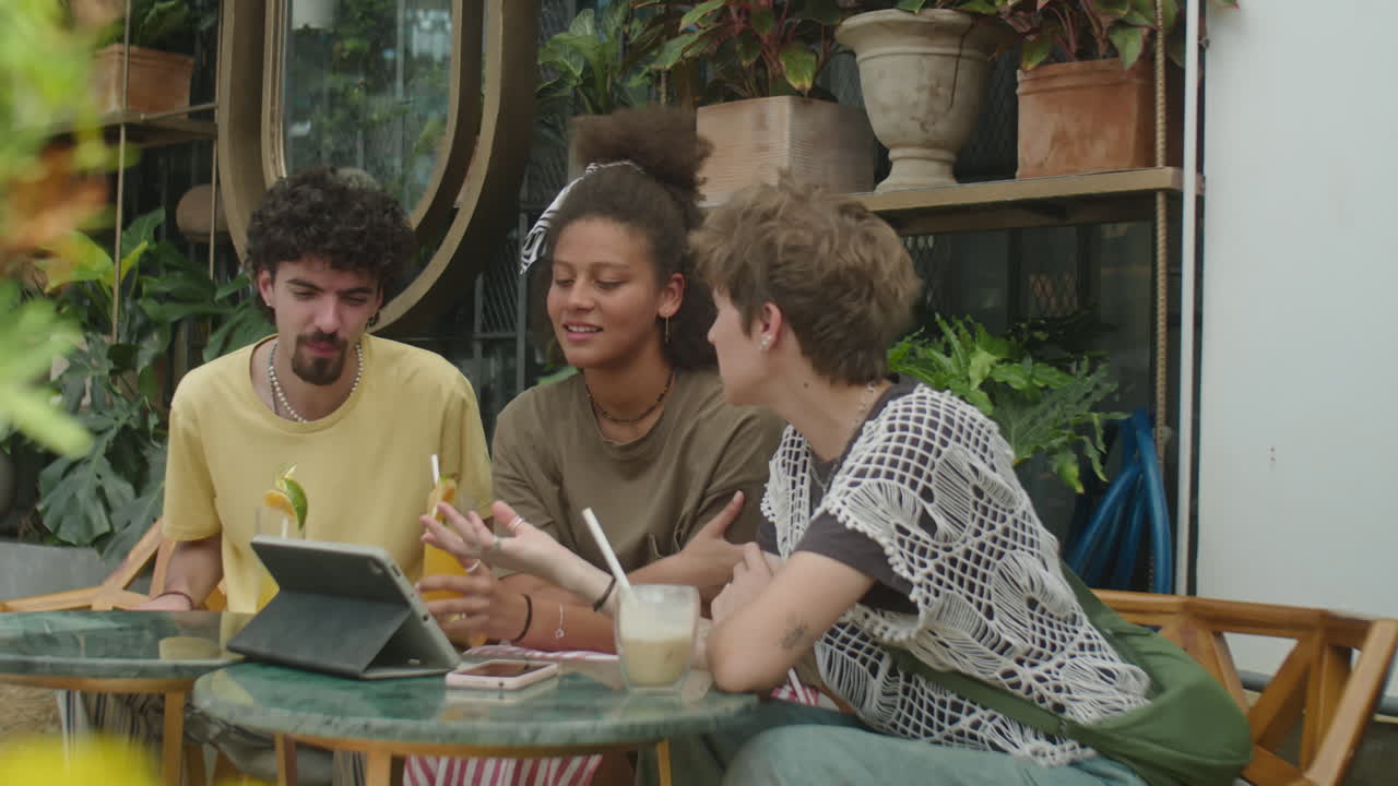 Friends Using Tablet and Chatting over Drinks in Outdoor Cafe