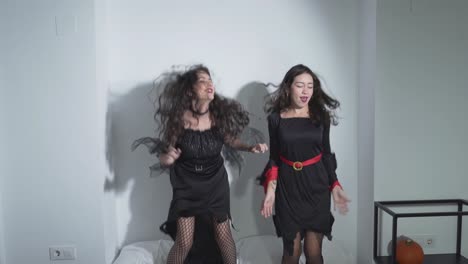 two women in halloween costumes dancing and jumping on a bed