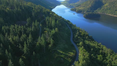 Carretera-Con-Coche-Siguiendo-La-Orilla-Del-Lago-Con-Vuelo-Sobre-Un-Bosque-De-Pinos-En-Una-Soleada-Mañana-De-Verano-En-Thirlmere,-English-Lake-District,-Cumbria,-Reino-Unido