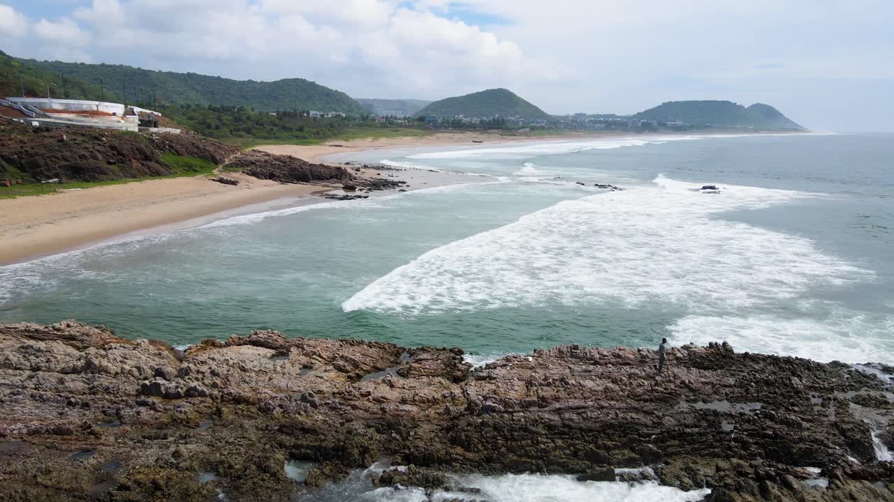 Stunning aerial drone shot of a rock formation rising from the ocean near Vizag, with the clear blue waters all around.
