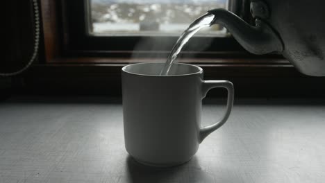 kettle pouring hot water into a mug and hand lifting mug