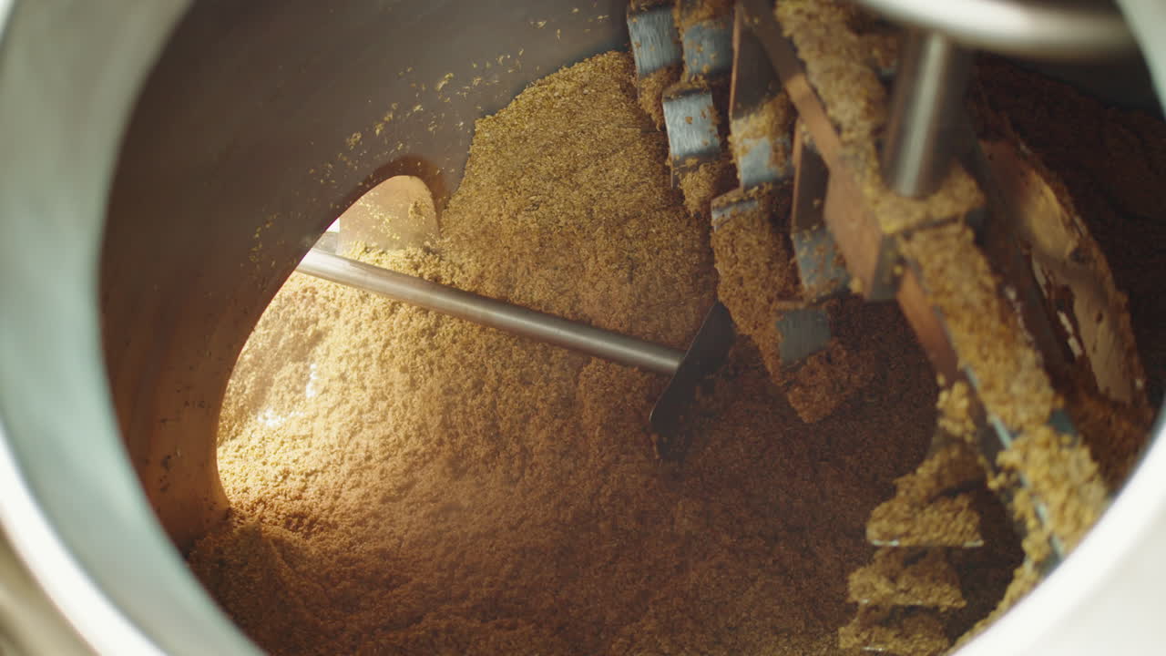 Craft beer production factory, brewery manufacture. Putting barley malt grains in conveyor close-up. Brewing, cooking alcohol in metal vats bottles