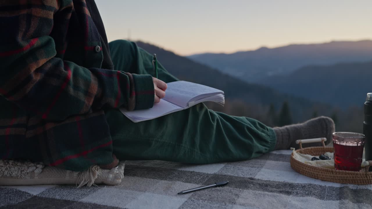 Person writing in a notebook in the mountains at sunset