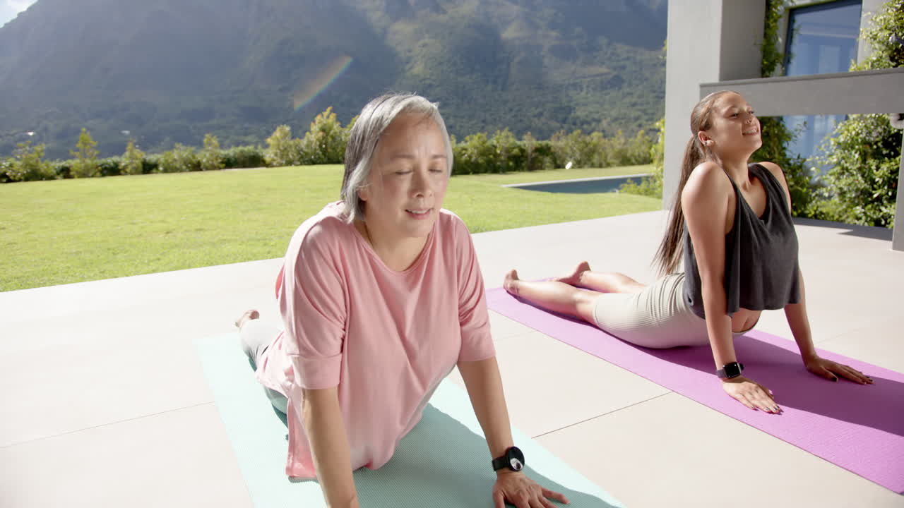 Practicing yoga, elderly woman and young woman stretching on yoga mats outdoors